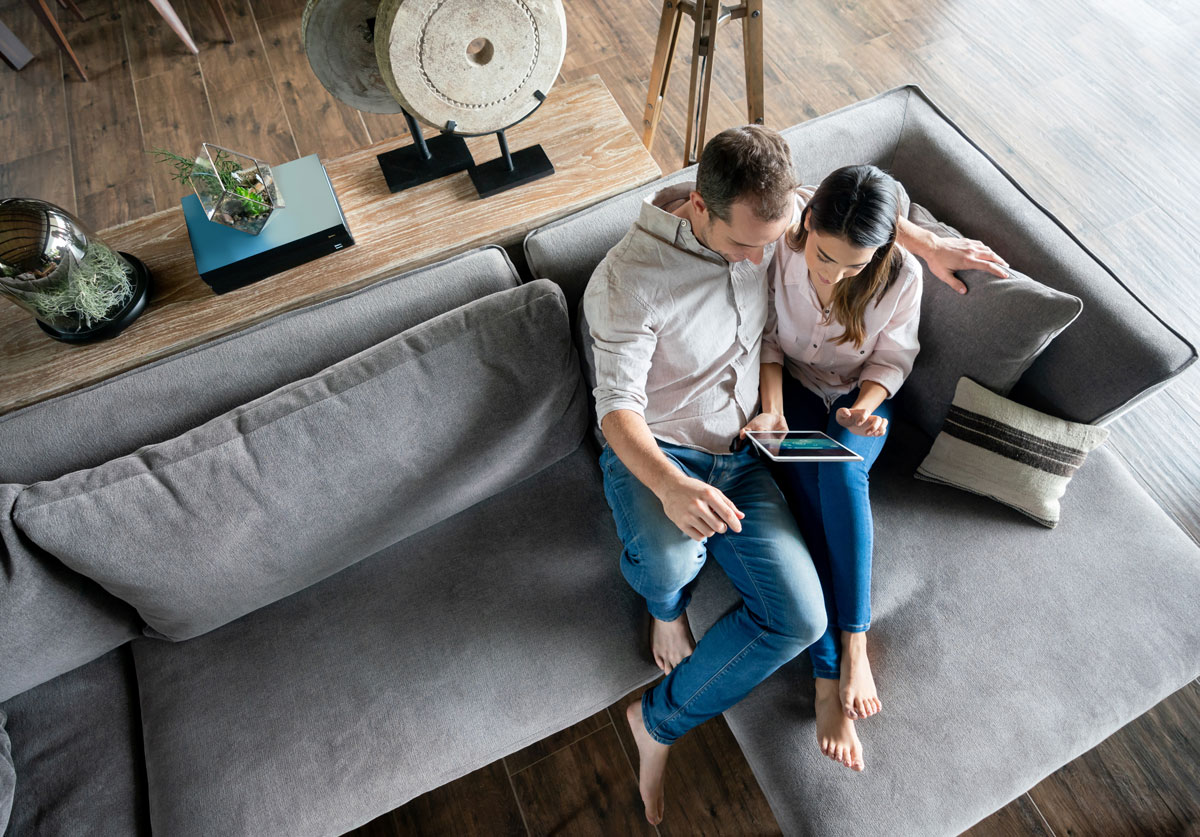 Engaged couple sitting on a couch, smiling and reviewing finances together.